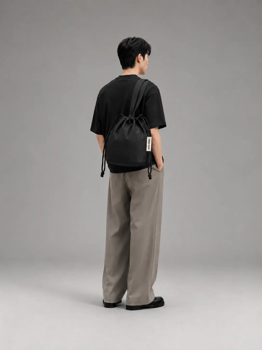 Model set bagfra iført sort T-shirt, grå bukser og sort skuldertaske i minimalistisk fashion styling