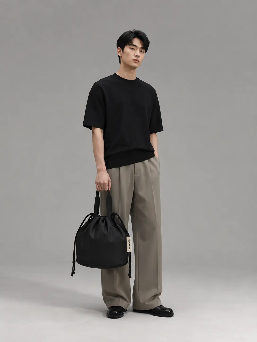 Model iført sort T-shirt og grå bukser med Nova Atelier Nivaro cinch pack i deep black holdt i hånden